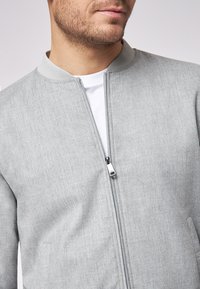 Giacca bomber grigia realizzata in tessuto morbido, con colletto alto, zip frontale e design minimalista senza motivi visibili.