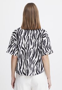 Camicetta a maniche corte a righe zebrate in bianco e nero, vestibilità ampia, con orlo dritto e dettaglio sul yoke posteriore. Tessuto leggero con una texture liscia.