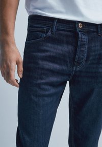 Mörkblå denimjeans med slim fit, med klassisk femfickdesign, subtila sömmar och ett enkelt knappstängning i midjan.