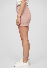 Lyserøde skræddersyede shorts med opviklede manchetter, lavet af et blødt stof, kombineret med hvide sneakers og et flettet bælte.