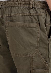 Olive green cargo pants with elastic waistband and multiple pockets, showing close-up of back and side pocket stitching details.