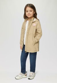 Beige hoodie met een gather taille, florale accenten, witte top, blauwe spijkerbroek en grijze sneakers met roze accenten. Gladde textuur, casual pasvorm.