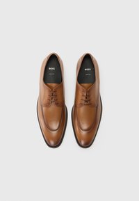 Zapatos oxford de cuero marrón con un acabado suave, puntera redondeada, diseño de cordones y un sutil logo en la plantilla. Suela de goma para mayor durabilidad.