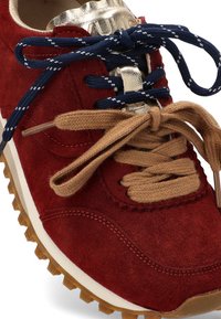 Zapatilla de ante rojo con doble cordón en azul con puntos blancos y marrón sólido, con suela de goma texturizada y detalle en la lengüeta dorada.