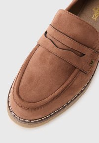 Mocassins en daim marron avec une finition lisse, présentant une couture, des découpes et un design à bout rond. Semelle en caoutchouc solide.