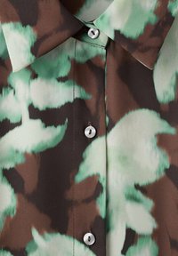 Camicia button-up con un motivo astratto verde e marrone, colletto a punta e bottoni bianchi lungo il davanti. Tessuto setoso.