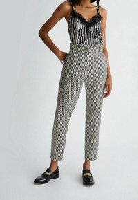 Zwart-witte outfit met een gestreepte top met kant en geometrisch patroon op de broek. Glanzende zwarte schoenen met gouden accenten.