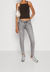 Top corto marrón oscuro, jeans ajustados grises, bolso blanco de hombro, zapatillas plateadas. Tejido suave, diseño ajustado, hardware mínimo.
