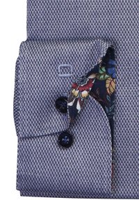 Polsino di camicia a quadri blu con interno a motivo floreale. Presenta una chiusura con bottone e dettagli ricamati. Tessuto testurizzato con colori a contrasto.