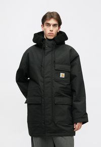 Must mustern jaakk, millel on tekstureeritud must fliisiga vooderdatud kapuuts, ees taskud ja logopatch. Omab sirget lõiget ja tõmblukke.