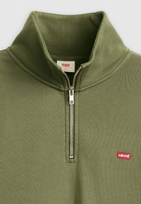 Olijfgroene fleece vest met rits en hoge kraag, zilveren rits en klein rood Levi's-logo op de linkerborst. Zachte textuur.