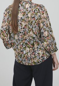 Blusa floreale con sfondo nero e grandi fiori rosa, bianchi e verdi. Maniche lunghe a sbuffo e design morbido.