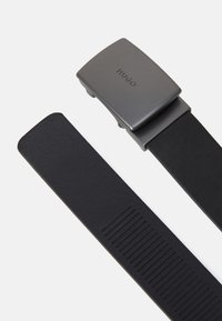 Sort læderbælte med en mat grå metal spænde, der har et logo og en tekstureret kant på remmen for ekstra grip.