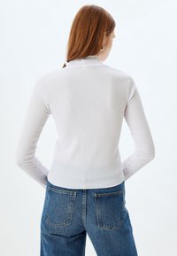 Jasnoszary, ribbed, długi top z wysokim dekoltem. Noszony z niebieskimi dżinsami, prezentującymi smukły krój i miękką teksturę.