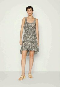 Vestido preto floral com alças finas, barra assimétrica, tecido leve, pequenas flores creme, acessórios com sandálias bejes.