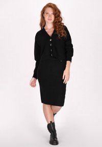 Completo due pezzi in maglia nera, composto da un cardigan corto con grandi bottoni e una gonna aderente. Il tessuto presenta un design testurizzato e dettagli a coste.