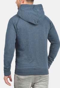 Sudadera azul con capucha, hecha de una tela suave, con mangas largas, puños acanalados y un dobladillo recto. Presenta un ajuste relajado y costuras sin costura.