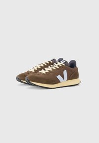 Brown suede sneakers with a mesh design, white "V" logo, cream laces, and a cushioned beige sole. Textured fabric and durable rubber outsole.
