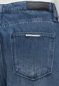 Πίσω τσέπη μπλε τζιν με ασημί και μαύρες ετικέτες της Karl Lagerfeld πάνω και επάνω στην τσέπη.