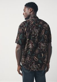 Chemise noire à manches courtes avec motifs floraux multicolores, présentant de grandes fleurs et feuilles, confectionnée en tissu léger.