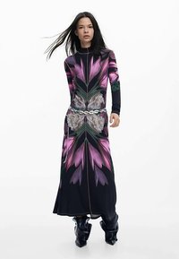 Robe maxi à manches longues avec un motif floral dans des tons de violet et de vert, dotée d'une fermeture éclair à l'avant et d'une ceinture argentée décorative. Confectionnée en tissu doux.