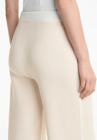 Pantalons larges beige en tissu doux texturé, avec une taille côtelée et un détail de bande latérale blanche.