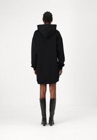 Vestido de moletom oversized preto com capuz, mangas longas, punhos canelados e bainha reta. Combinado com botas pretas brilhantes até ao joelho.