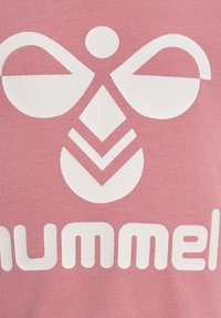 Rosa rippenstrukturierter Stoff mit einem auffälligen weißen grafischen Design, das Formen wie Kreise und Dreiecke umfasst, mit dem Text "hummel" darunter.