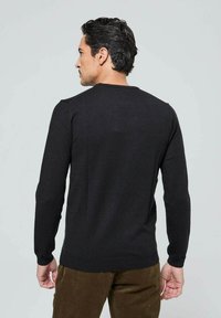 Pull en maille noir avec des manches longues et un col rond, présenté de dos. Il présente une texture lisse et une coupe ajustée.