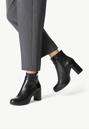 Botines de cuero negro hasta el tobillo con un tacón gordo, que presentan una cremallera lateral, detalles de correa ajustable y una textura suave y brillante.