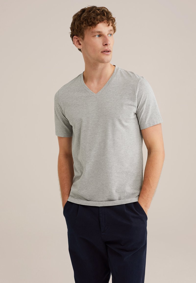 Camiseta gris de cuello en V hecha de tela suave, con mangas cortas y un ajuste relajado, combinada con pantalones azul marino. Diseño simple, sin patrones notables.
