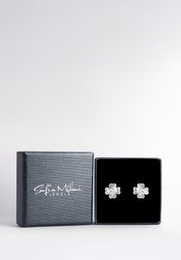 Söta silverblommiga stiftörhängen visade i en svart sammetfodrad låda med en strukturerad svart ytbehandling och vit logotyp.