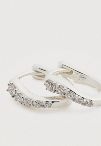 Cercei rotunzi din argint cu un design ondulat, având pietre prețioase mici, rotunde și clare, așezate pe partea din față pentru un plus de detaliu.