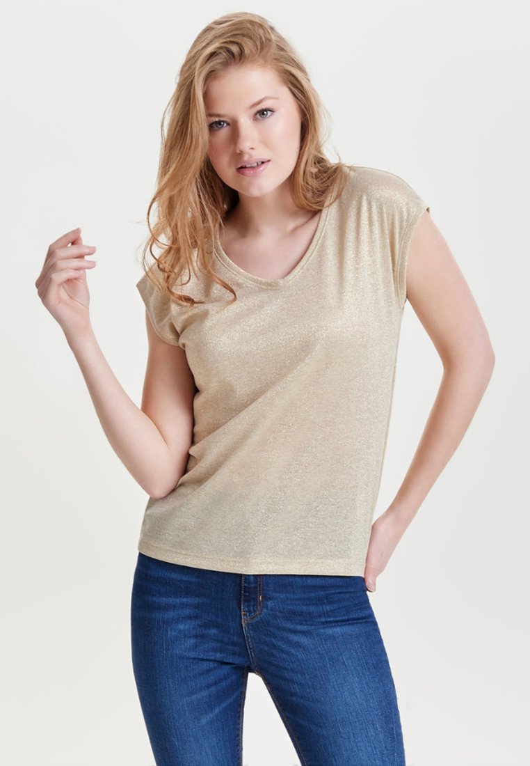 Gul, kortærmet V-hals t-shirt med en blød, skinnende tekstur. Parret med blå denim jeans. Modellen poser med en hånd hævet.