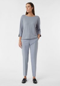 Haut en tricot côtelé gris clair à manches trois-quarts, associé à un pantalon gris clair ajusté et des mocassins noirs. Design simple et structuré.
