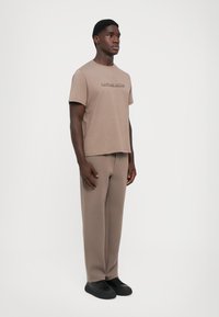 Brun bomull crew neck t-skjorte med preget logo. Kombinert med matchende brune bomullssweatpants og svarte snørestøvler.