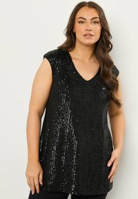 Top nero senza maniche con scollo a V, impreziosito da paillettes verticali per un effetto tridimensionale. Il tessuto cade in modo morbido sul corpo.