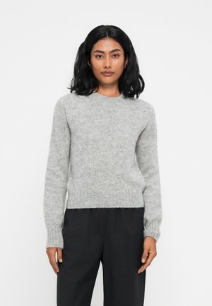 Grå strikket sweater med rund halsudskæring, lange ærmer og ribbede manchetter og kant. Blød tekstur, afslappet pasform, parret med mørke bukser.