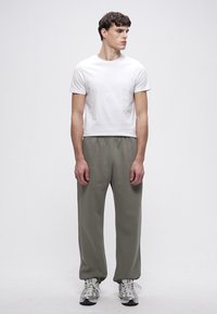 Weißes T-Shirt mit Rundhalsausschnitt und lockere olivgrüne Sweatpants mit elastischem Bund, kombiniert mit grauen und weißen Sportschuhen.