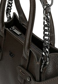 Ciemnobrązowa skórzana torba o fakturowanym wykończeniu, wyposażona w podwójne uchwyty i metalowy łańcuszek jako ozdobę. Zamek błyskawiczny i detal z logo.