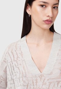 Hellgrauer, gestrickter Pullover mit V-Ausschnitt, der ein strukturiertes, offenes Design aufweist. Kurze Ärmels sowie weicher Stoff mit glatter Oberfläche.