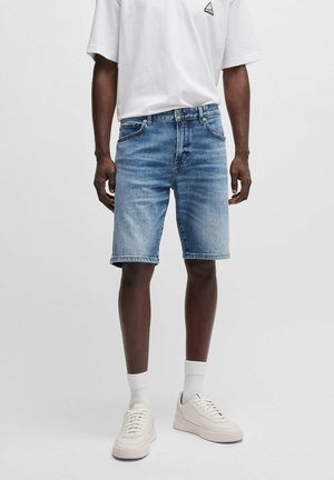 Ljust blå denimshorts med klassisk snitt, något fransade kanter, bärs med en vit t-shirt och krämfärgade sneakers. Enkelt design, utan mönster.