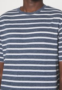 Námořnické pruhované tričko s alternativními horizontálními bílými pruhy, vyrobené z měkkého materiálu, s klasickým kulatým výstřihem a krátkými rukávy.