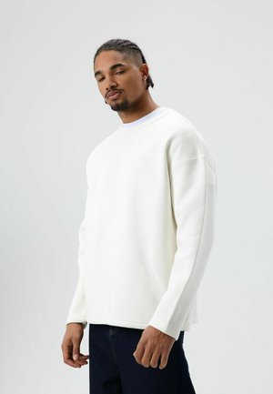 Witte sweatshirt met een ontspannen pasvorm, ronde hals, lange mouwen en een zachte textuur. Gecombineerd met donkere jeans voor contrast.