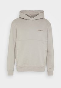 Beige Hoodie aus weichem Stoff, mit Kängurutasche, gerippten Bündchen und einem dezenten, aufgestickten Logo auf der Brust.