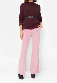 Vindrød strikbluse lagdelt over en bordeaux skjorte, kombineret med flagrende lyserøde manchetbukser i ribstof og sorte ankelstøvler med hæl.