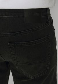 Černé džíny z denimu s kapsou vzadu a štítkem značky Hollister California na pásu, nošené s bílým topem.