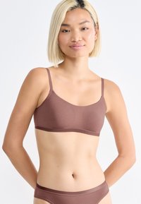 Hnědý bezšvový bralet s tenkými nastavitelnými ramínky a hladkým povrchem. Jednoduchý design, bez ozdob či vzorů.