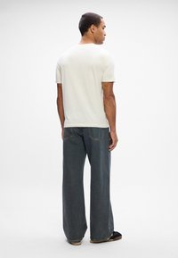 Hvid kortærmet t-shirt parret med mørkeblå brede jeans. Jeansene har en kontrasterende gul syning og baglommer.