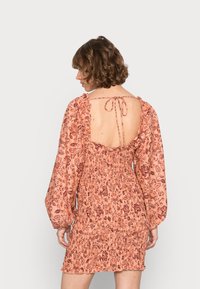 Vestido mini de tecido com padrão floral em pêssego claro, com mangas longas bufantes, costas abertas e fecho ajustável com laço. Detalhe de tecido texturizado.